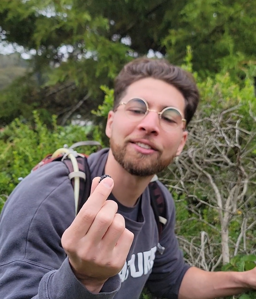 Nick leaning forward grinning and holding a tiny wild blackberry toward the camera